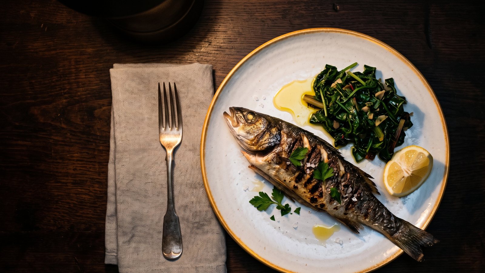 Gegrilde vis, groenten en olijfolie op een bord onder één warme lamp